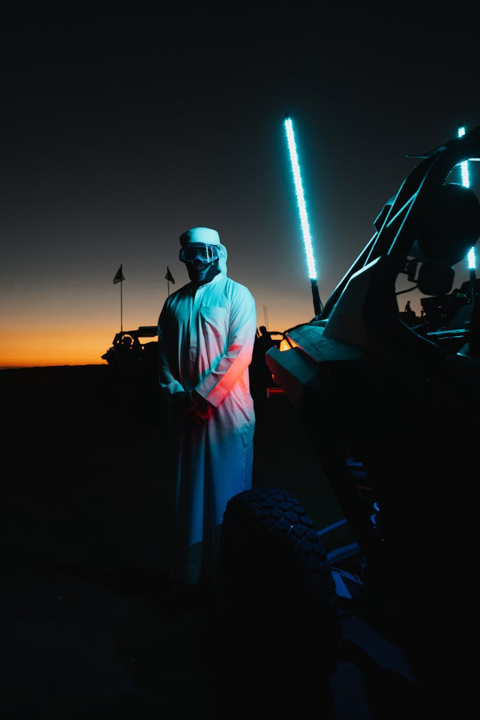 A man stands beside an off-road vehicle in the Dubai desert at sunset.